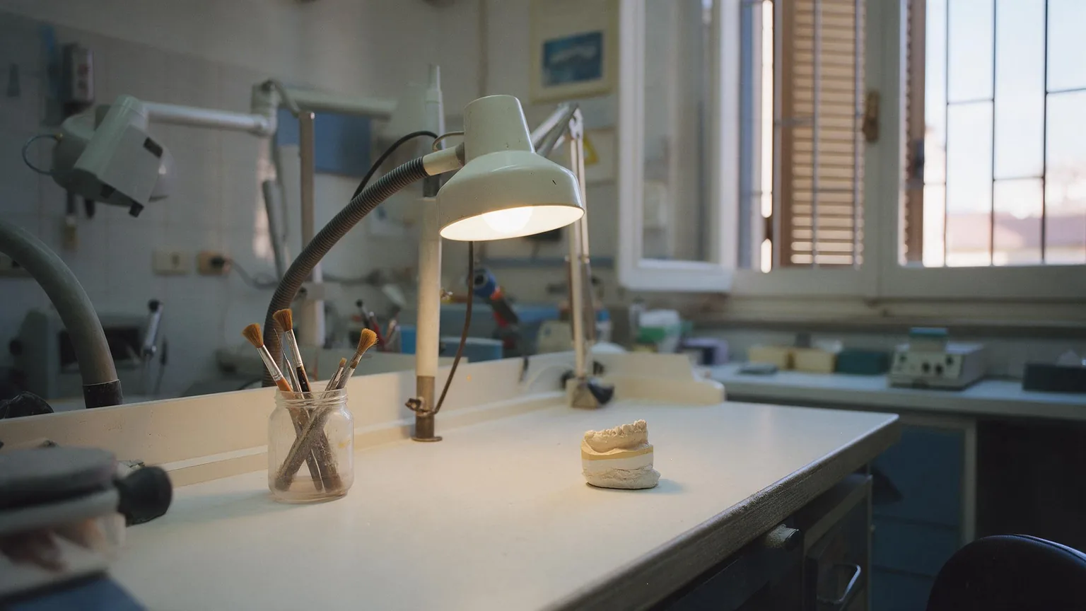 Banco di lavoro vuoto illuminato da una lampada, con pennelli in un barattolo e un modello in gesso